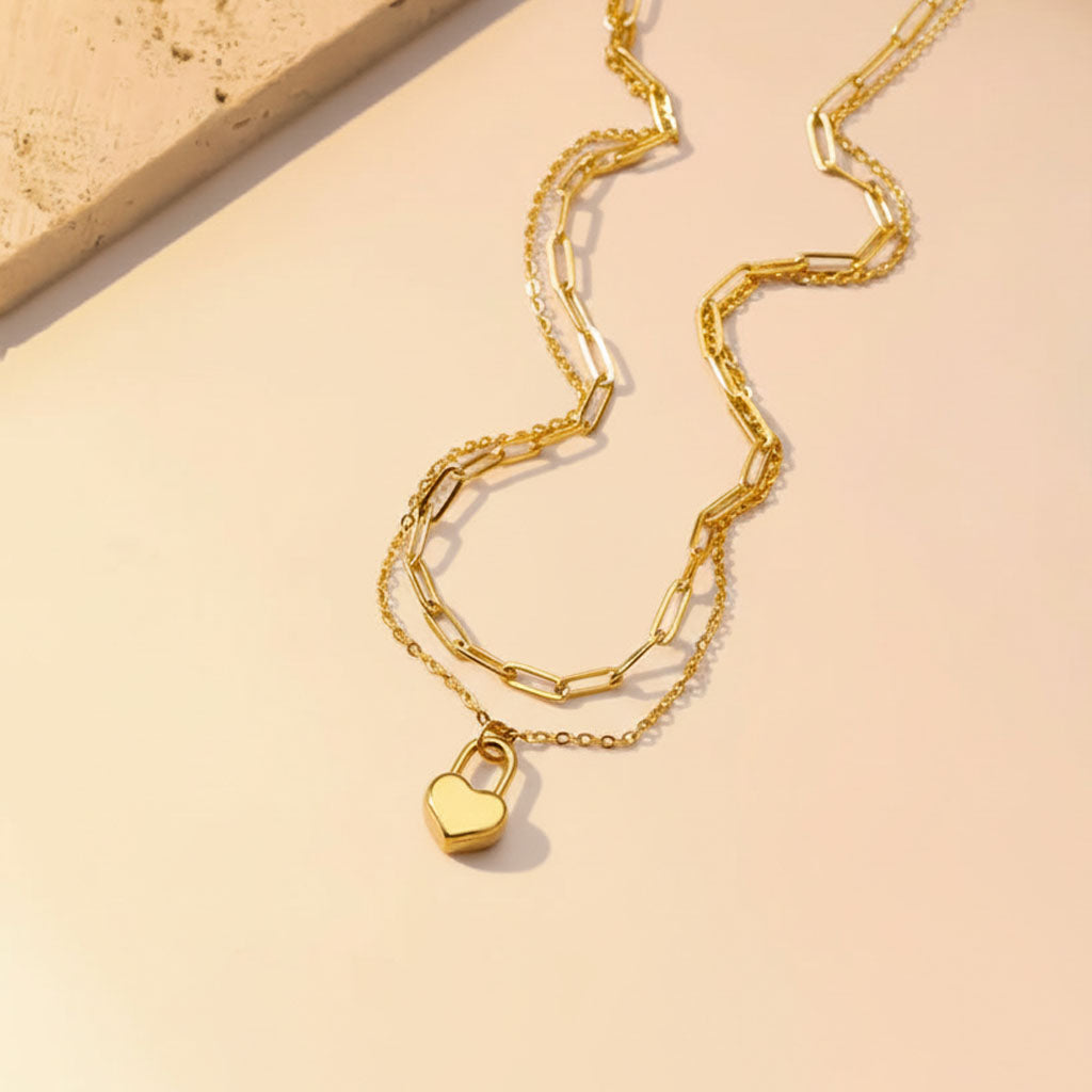 Gold chain necklace with a heart-shaped lock pendant on a beige background